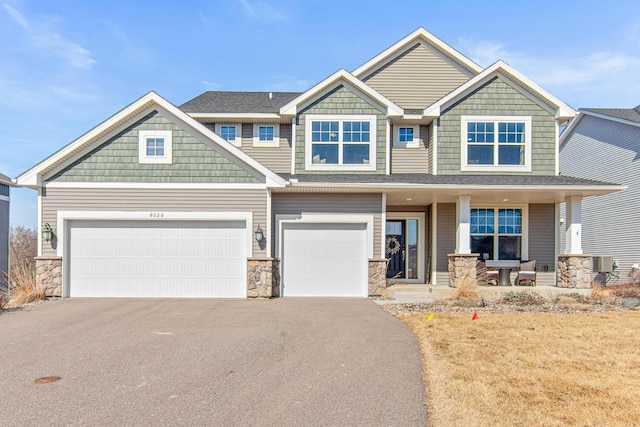 craftsman inspired home with aphalt driveway, stone siding, covered porch, and central AC unit