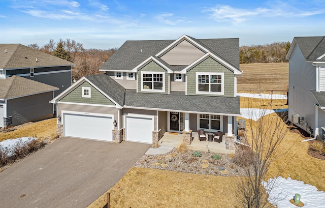 craftsman-style home featuring driveway, a porch, a shingled roof, a garage, and stone siding