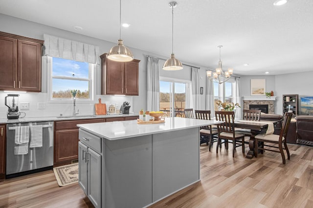 kitchen featuring light wood finished floors, a sink, a kitchen island, light countertops, and dishwashing machine