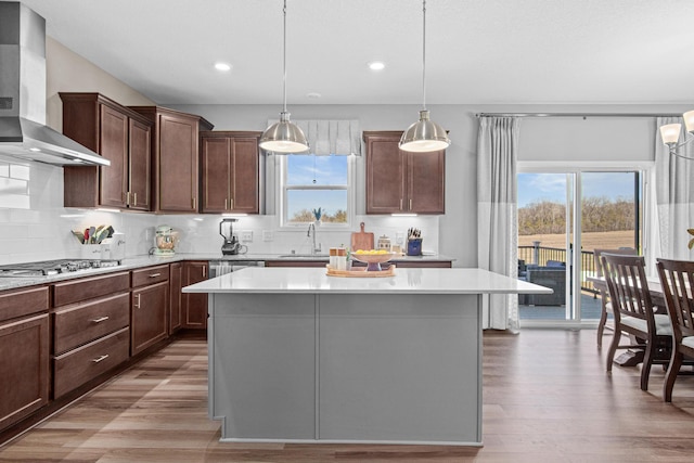 kitchen featuring a kitchen island, wall chimney range hood, light countertops, stainless steel gas stovetop, and a sink