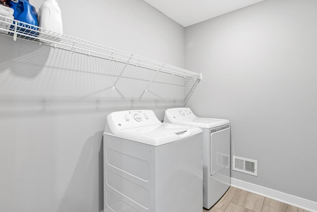 washroom with light wood finished floors, visible vents, baseboards, laundry area, and washer and dryer