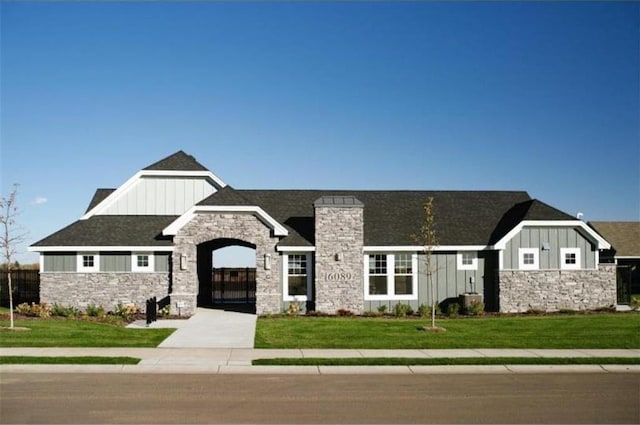 view of front of house with board and batten siding, a shingled roof, fence, a front yard, and stone siding