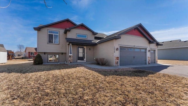 view of front of home with stone siding, driveway, a front yard, and an attached garage