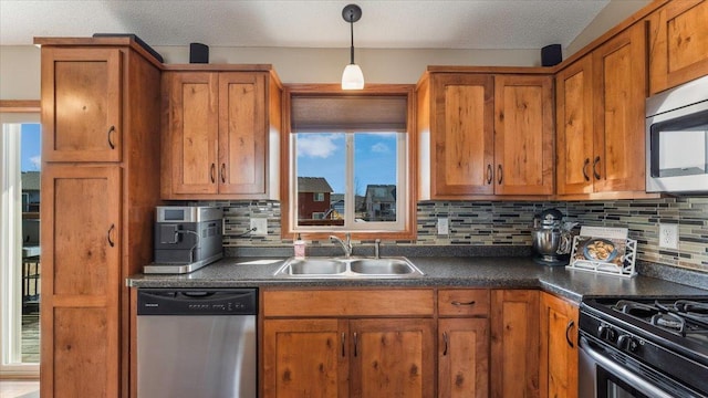 kitchen featuring brown cabinetry, a sink, appliances with stainless steel finishes, pendant lighting, and dark countertops