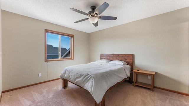 bedroom featuring light colored carpet, a textured ceiling, baseboards, and a ceiling fan