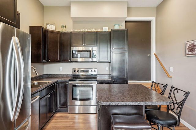 kitchen with light wood-type flooring, a sink, a kitchen breakfast bar, stainless steel appliances, and dark brown cabinetry