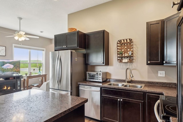 kitchen with a sink, a lit fireplace, stainless steel appliances, dark brown cabinets, and dark countertops