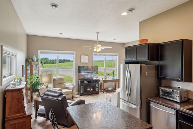 kitchen with a toaster, open floor plan, a warm lit fireplace, a textured ceiling, and stainless steel appliances