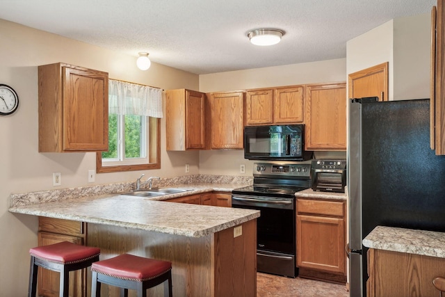 kitchen featuring a peninsula, freestanding refrigerator, a sink, range with electric cooktop, and black microwave