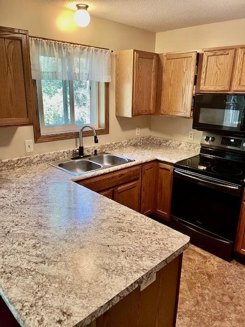 kitchen with black appliances, light countertops, a peninsula, a textured ceiling, and a sink