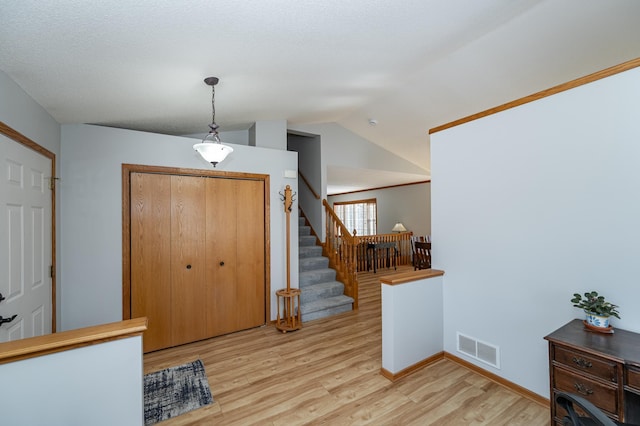 entrance foyer with visible vents, baseboards, stairway, lofted ceiling, and light wood-style flooring