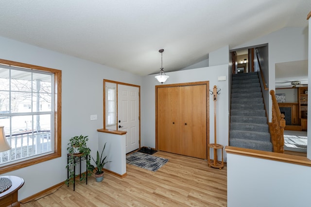 entryway with stairs, vaulted ceiling, light wood-style flooring, and baseboards