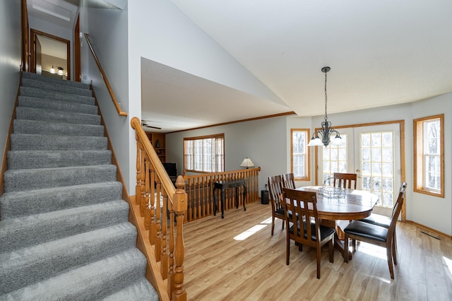 dining area with light wood finished floors, crown molding, stairs, lofted ceiling, and a notable chandelier