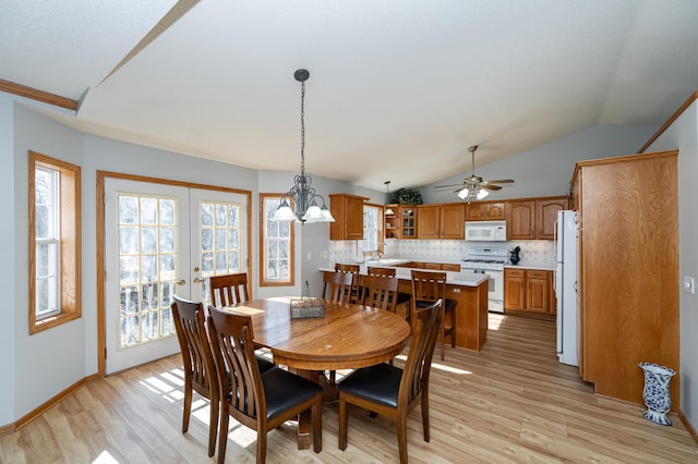 dining area with ceiling fan with notable chandelier, lofted ceiling, light wood-style flooring, and french doors