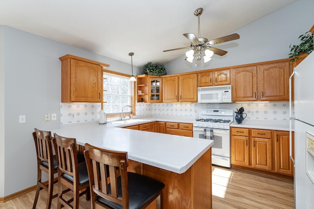 kitchen featuring tasteful backsplash, a kitchen breakfast bar, a peninsula, white appliances, and a sink