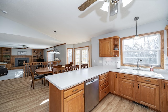 kitchen featuring a fireplace with raised hearth, a sink, stainless steel dishwasher, open floor plan, and light countertops