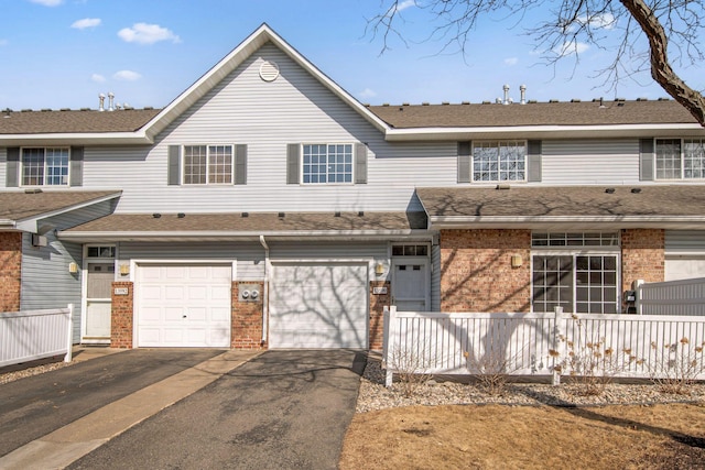 multi unit property featuring brick siding, an attached garage, driveway, and roof with shingles