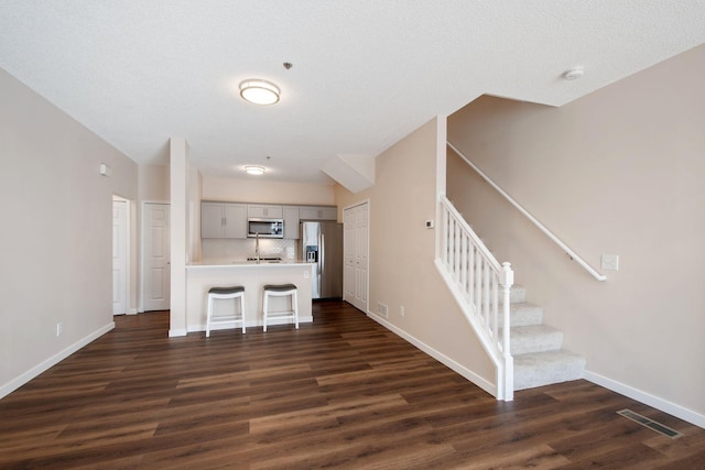 kitchen featuring visible vents, dark wood-style flooring, light countertops, appliances with stainless steel finishes, and a kitchen bar