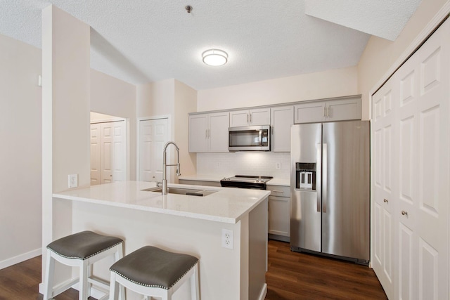 kitchen featuring a sink, a kitchen bar, appliances with stainless steel finishes, and gray cabinets