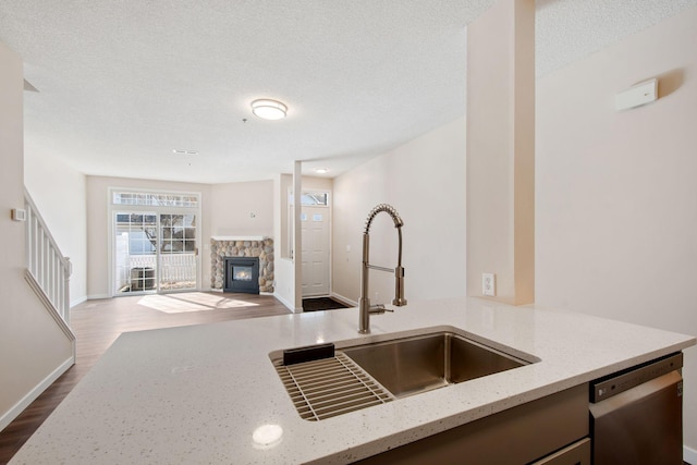 kitchen with light stone counters, a fireplace, a sink, dark wood-type flooring, and stainless steel dishwasher