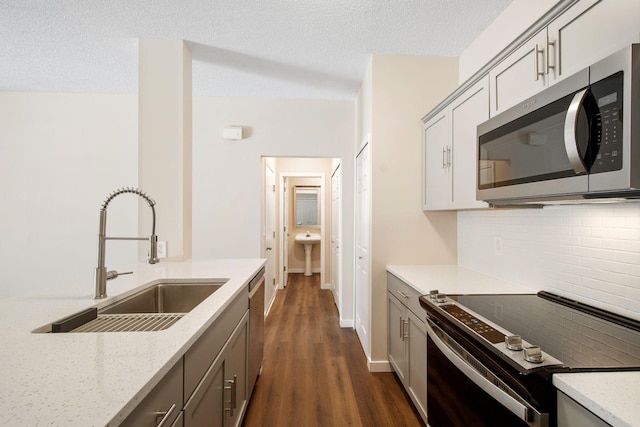 kitchen with gray cabinetry, a sink, backsplash, dark wood-style floors, and stainless steel appliances