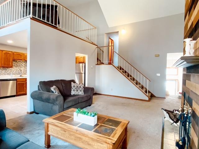 living area with stairway, light carpet, a high ceiling, and a tile fireplace