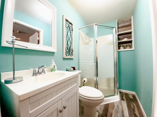 bathroom with toilet, a stall shower, wood finished floors, baseboards, and vanity