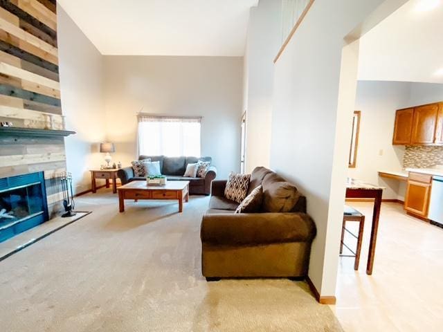 living area featuring a stone fireplace, light colored carpet, and a towering ceiling