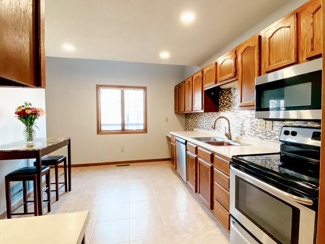 kitchen featuring a sink, backsplash, appliances with stainless steel finishes, light countertops, and baseboards