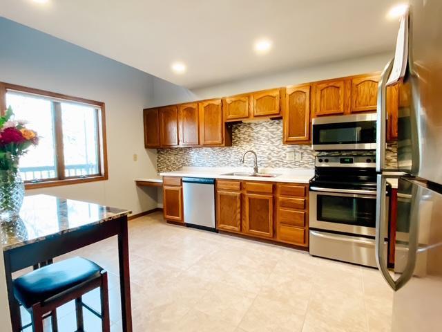 kitchen featuring a sink, tasteful backsplash, appliances with stainless steel finishes, brown cabinetry, and light countertops