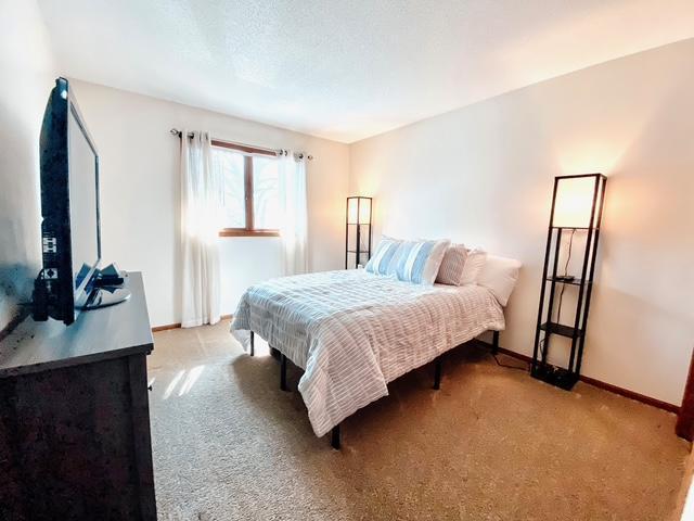 bedroom featuring baseboards, light colored carpet, and a textured ceiling