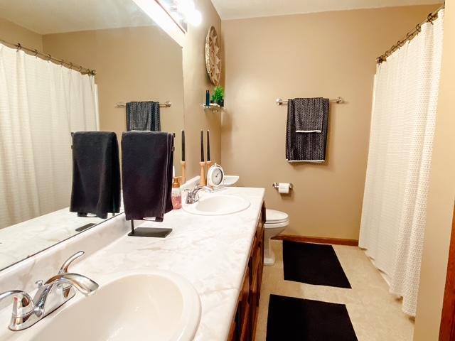 full bath featuring double vanity, toilet, baseboards, and a sink