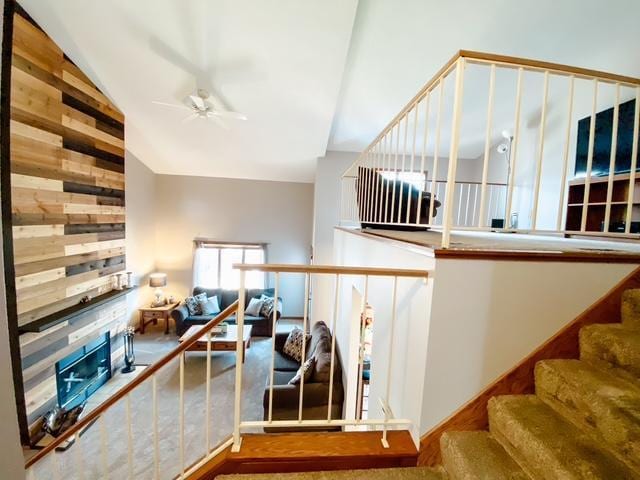 stairs with wooden walls, a fireplace, lofted ceiling, and a ceiling fan