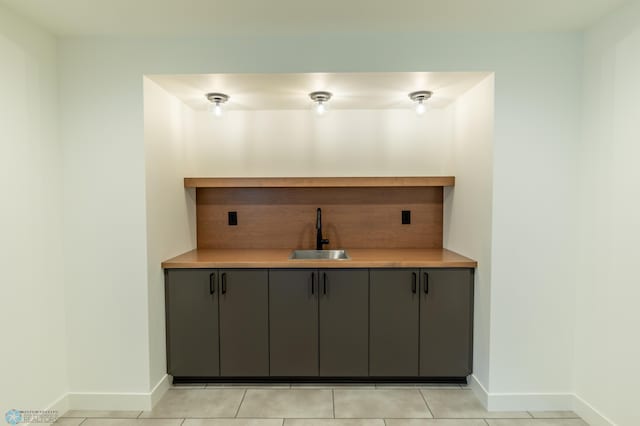 bar featuring baseboards, a sink, wet bar, and light tile patterned flooring