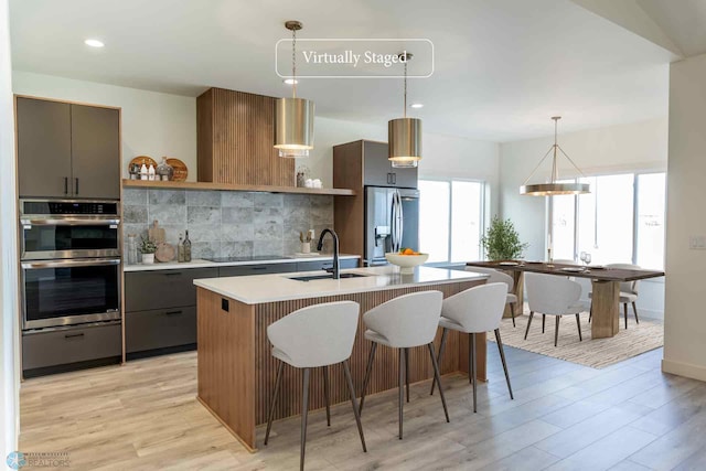 kitchen featuring light countertops, a sink, open shelves, appliances with stainless steel finishes, and decorative backsplash