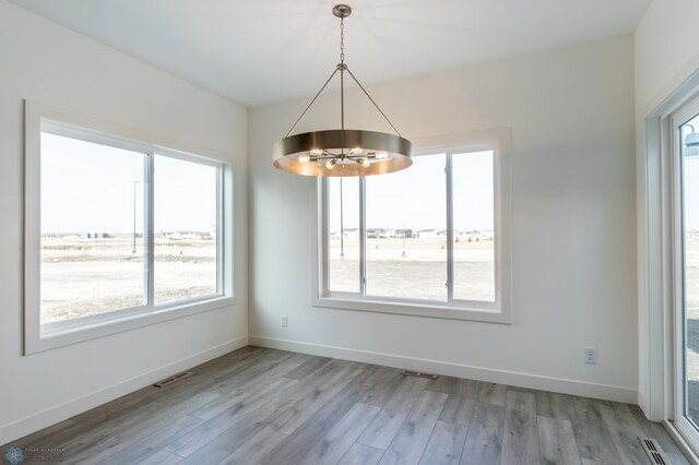 unfurnished dining area with baseboards, visible vents, light wood-style flooring, and an inviting chandelier