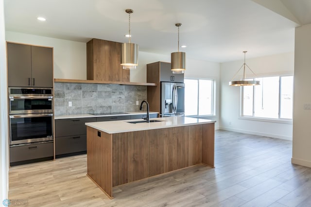 kitchen featuring light countertops, modern cabinets, appliances with stainless steel finishes, a sink, and backsplash