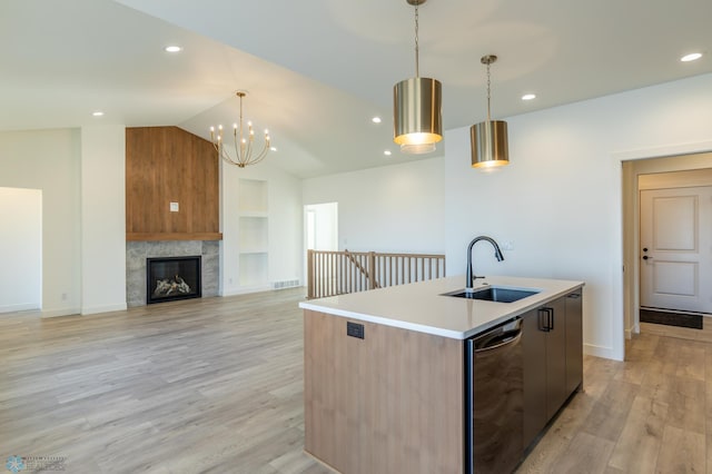 kitchen with light wood-style flooring, a center island with sink, a sink, dishwashing machine, and built in features