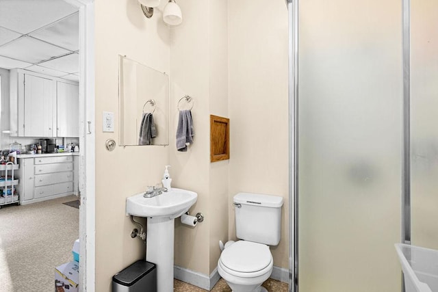 full bathroom featuring a drop ceiling, toilet, baseboards, and a shower with shower door