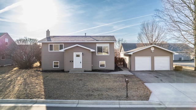 bi-level home featuring a garage, an outbuilding, a chimney, and a shingled roof