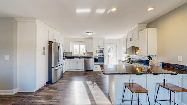 kitchen featuring stainless steel appliances, a peninsula, dark wood-style flooring, and white cabinetry