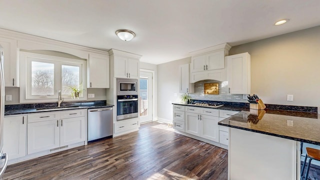 kitchen with dark wood-style floors, a peninsula, a sink, stainless steel appliances, and white cabinets