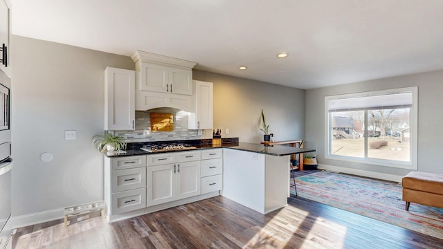 kitchen featuring decorative backsplash, a peninsula, stainless steel gas stovetop, white cabinets, and dark wood-style flooring