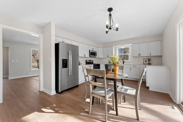 kitchen featuring an inviting chandelier, backsplash, light wood finished floors, and stainless steel appliances