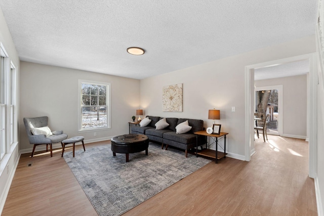 living area with light wood-style flooring, a textured ceiling, and baseboards