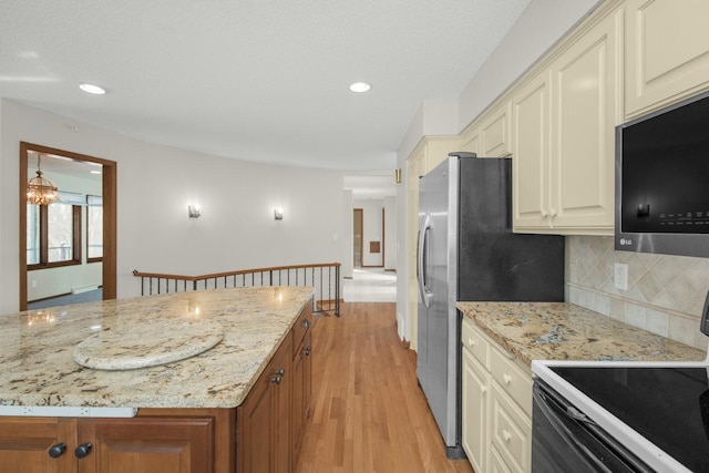 kitchen with electric stove, stainless steel microwave, tasteful backsplash, light wood-style floors, and light stone countertops