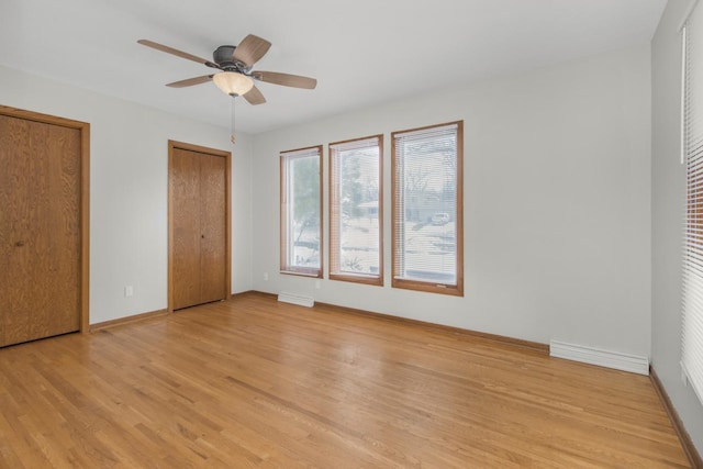 unfurnished bedroom featuring light wood-style flooring, two closets, baseboards, and ceiling fan