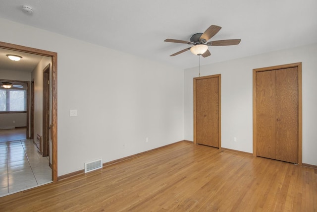 unfurnished bedroom featuring light wood-type flooring, visible vents, baseboards, and two closets