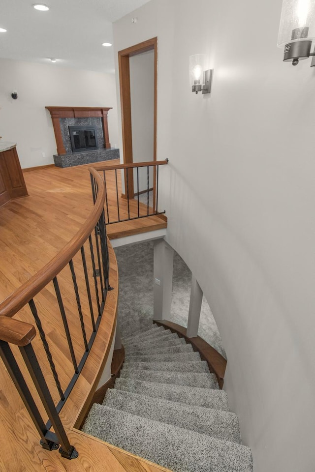 staircase featuring a glass covered fireplace, recessed lighting, and wood finished floors