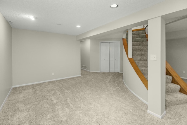 finished below grade area featuring stairway, visible vents, baseboards, and carpet